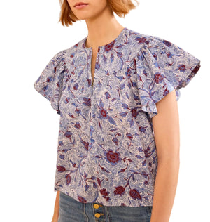 A woman wears the Ulla Johnson Perline Blouse, a short-sleeve floral poplin top with flutter sleeves and a round neckline, paired with high-waisted jeans.