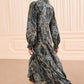 A woman wearing a long-sleeved, ankle-length Sabrina Silk Dress by Ulla Johnson with subtle ruffle details and tan heeled boots walks away in a beige room with vertical wall paneling.