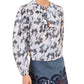 A woman wears the Ulla Johnson Siena Top, a relaxed-fit, long-sleeve patterned blouse with ruffle details, paired with a blue mini skirt featuring decorative cut-out designs at the hem.