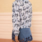 A woman stands with her back to the camera, wearing Ulla Johnson’s relaxed-fit Siena Top in a blue patterned cotton-blend and a denim skirt featuring dark blue scalloped trim.