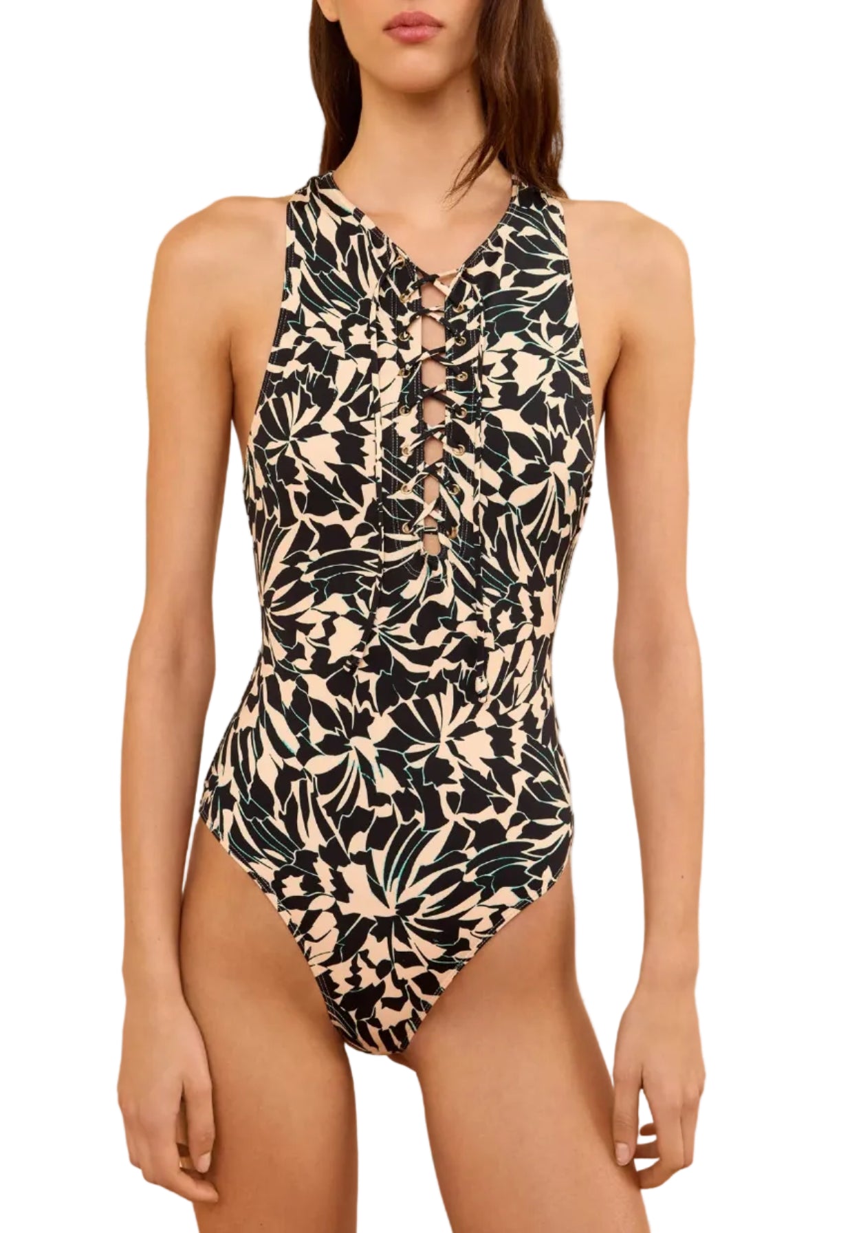 A woman wears the Ulla Johnson Solina One Piece, a black and beige swimsuit featuring vibrant floral motifs and front lace-up detailing, standing against a white background.