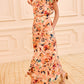 A person wearing the Ulla Johnson Sophea Skirt in a peach-colored botanical print stands in a beige paneled room, paired with gold sandals on a patterned carpet.