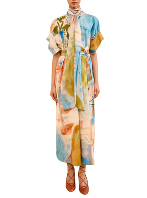 A model wears the Ulla Johnson Studio Dress, showcasing abstract prints, a belted waist, short sleeves, and a long neck tie, paired with brown lace-up heels against a white background.