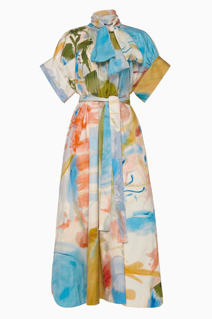 The Studio Dress by Ulla Johnson is a midi-length design with colorful abstract print, short sleeves, a high neck with bow detail, and a matching fabric belt.