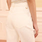 Model wearing the Ulla Johnson Lou Eyelet Jean—a cream-colored, vintage-inspired flared pant with visible pockets and belt loops—paired with a sleeveless top, shown from the back.