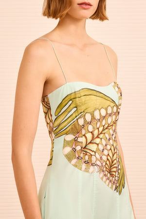 A woman wears the Vesela Cami Midi Dress by Ulla Johnson, a light blue poplin dress with thin straps and an abstract multicolored hand and shell pattern on the bodice inspired by Anna Zemánková’s imaginative style.