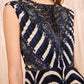 A woman wearing the Ulla Johnson Violeta Pleated Midi Dress, featuring a sleeveless design and geometric navy, white, and black pattern with subtle pleats, stands in front of a light wooden background.