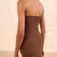 Wearing the Yanni Strapless Knit Top by Ulla Johnson, a person stands in a room with cream-colored, paneled walls.