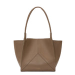 The Victoria Beckham Victoria Tote is a taupe leather handbag with two handles, a geometric front panel, an embossed logo at the bottom center, and a suede-lined interior.