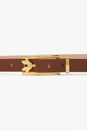 The Victoria Beckham Pin Buckle Dorian Belt, crafted from dark tan calf leather and featuring a gold, stylized pin buckle, is displayed against a plain white background.