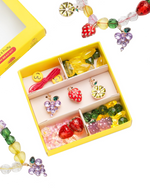 The Make It Fruity Mini Bead Kit by Super Smalls features colorful fruit-inspired charms and berry-bright beads—strawberries, grapes, lemons, and smiley faces—all neatly organized in compartments.