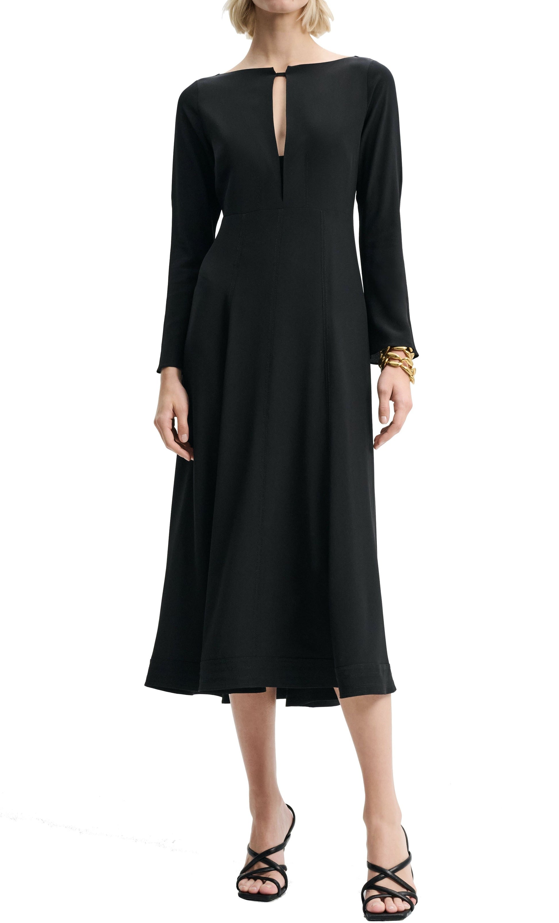 Person wearing a long-sleeved, black midi-length Dorothee Schumacher Sophisticated Volumes Dress with a front keyhole cutout, black strappy sandals, and a gold bracelet on the left wrist.