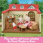Three rabbit figurines relax in a cozy living room furnished with the Calico Critters Comfy Living Room Set inside a toy house featuring a red roof, wooden furniture, and a TV. Text at the bottom reads: “Play together with homes including the Sweet Raspberry Home.”.