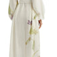 A person seen from the back wears the Erdem Long Sleeve Midi Dress With Tie Waist Detail, a white linen dress with botanical prints and long sleeves, paired with lace-up espadrille sandals.