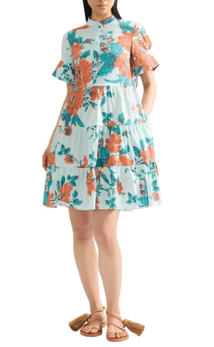 Someone wearing Erdem's Trailing Poppy Short Shirt Dress, a short-sleeve mini dress featuring an orange and teal poppy print, paired with tan tassel sandals.