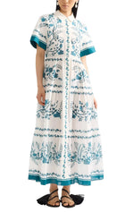 A woman wears the Erdem Wild Fern Botanical Shirt Dress, an ankle-length cotton linen-blend with blue fern print, short sleeves, teal trim, styled with black sandals.