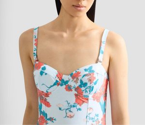 A woman wears the Erdem Trailing Poppy One Piece, a light blue floral swimsuit with moulded cups, thin straps, and a sweetheart neckline, shown from shoulders to mid-torso.
