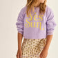 A young girl wears the Cozmo Girls' Vega Sweatshirt with a crew neckline and "Yes Sun" in yellow, paired with a beige floral skirt, as she stands slightly turned to the side.