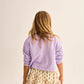 A young girl faces away, wearing the Cozmo Girls' Vega Sweatshirt in light purple with a crew neckline and a cream ruffled floral skirt, set against a plain background.