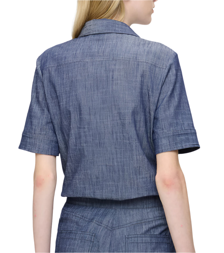 A person wearing the Vesper Top by Callas Milano is turned away, showcasing its retro charm with an indigo denim short-sleeve design.