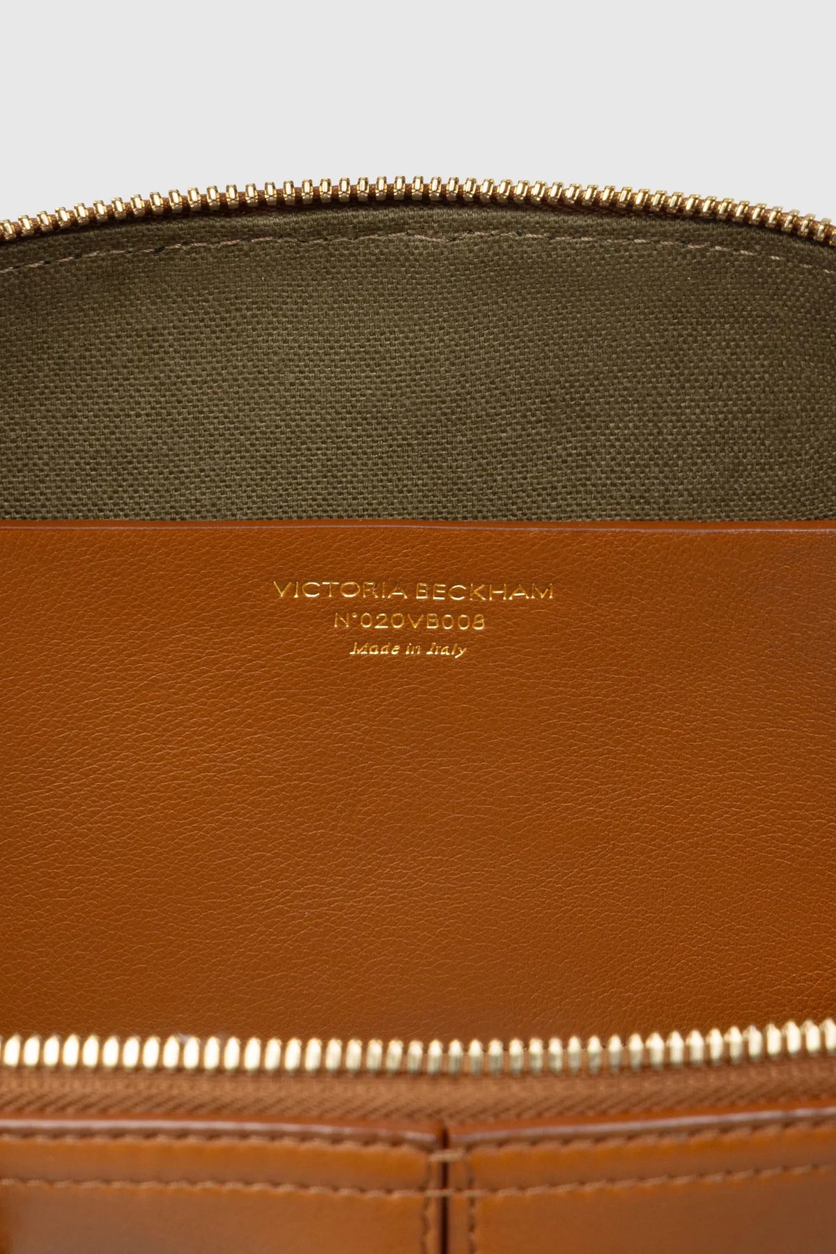 Close-up of a brown leather Victoria Small Doctor Bag interior by Victoria Beckham, featuring a gold zipper, embossed text, and crossbody strap attachment space.