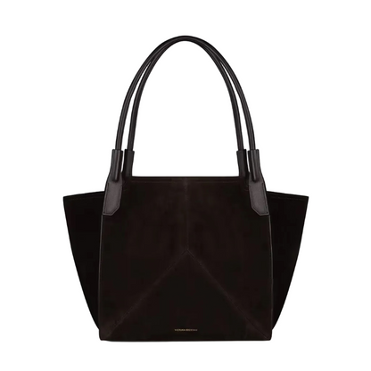 The Victoria Suede Tote by Victoria Beckham features two handles, a structured shape for laptops, and subtle gold text near the base, shown on a plain white background.