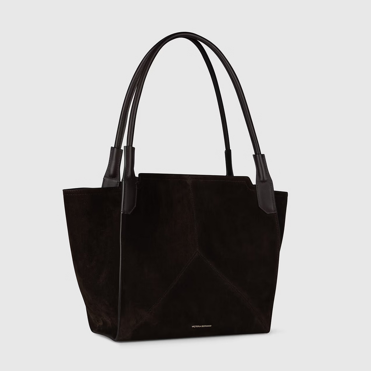 The Victoria Suede Tote by Victoria Beckham features black suede and two long black leather handles, shown on a light gray background.