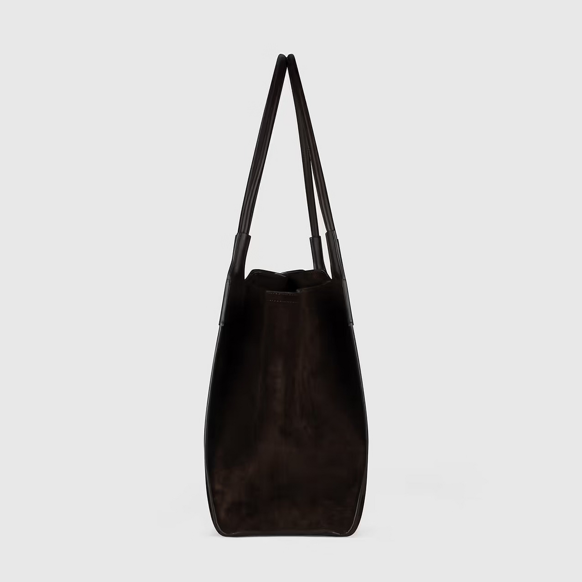 The Victoria Suede Tote by Victoria Beckham is a dark brown suede shoulder bag with two handles and a minimalist side profile against a plain light background.
