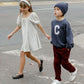 Two children cross a street; the girl wears Rylee & Cru’s Girls' Sabrina Mini Dress with a headband, while the boy wears a beanie, dark sweatshirt with a "C," and maroon pants.