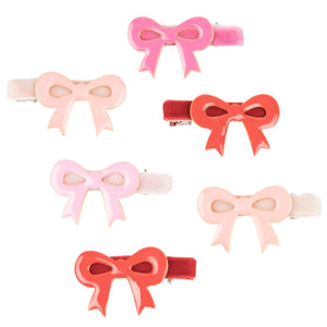 The Meri Meri Valentine's Bow Hair Clips, a set of six charming enamel clips in pink, red, and peach shades, are perfectly arranged in two rows on a white background, making them an ideal Valentine's Day accessory.