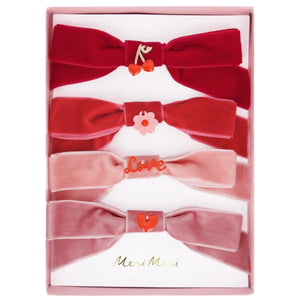 Gift a Valentine's treasure: the "Meri Meri Velvet Bows with Charms Hair Clips" set, featuring five velvet bow hair clips in red and pink, each with a romantic charm, elegantly packed in a pink box.