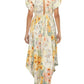 A person wears the Aire Maxi Dress by Agua By Aguabendita, a floral maxi dress with an open back and puffed sleeves, adorned with hand-embroidered details, standing with their back to the camera.