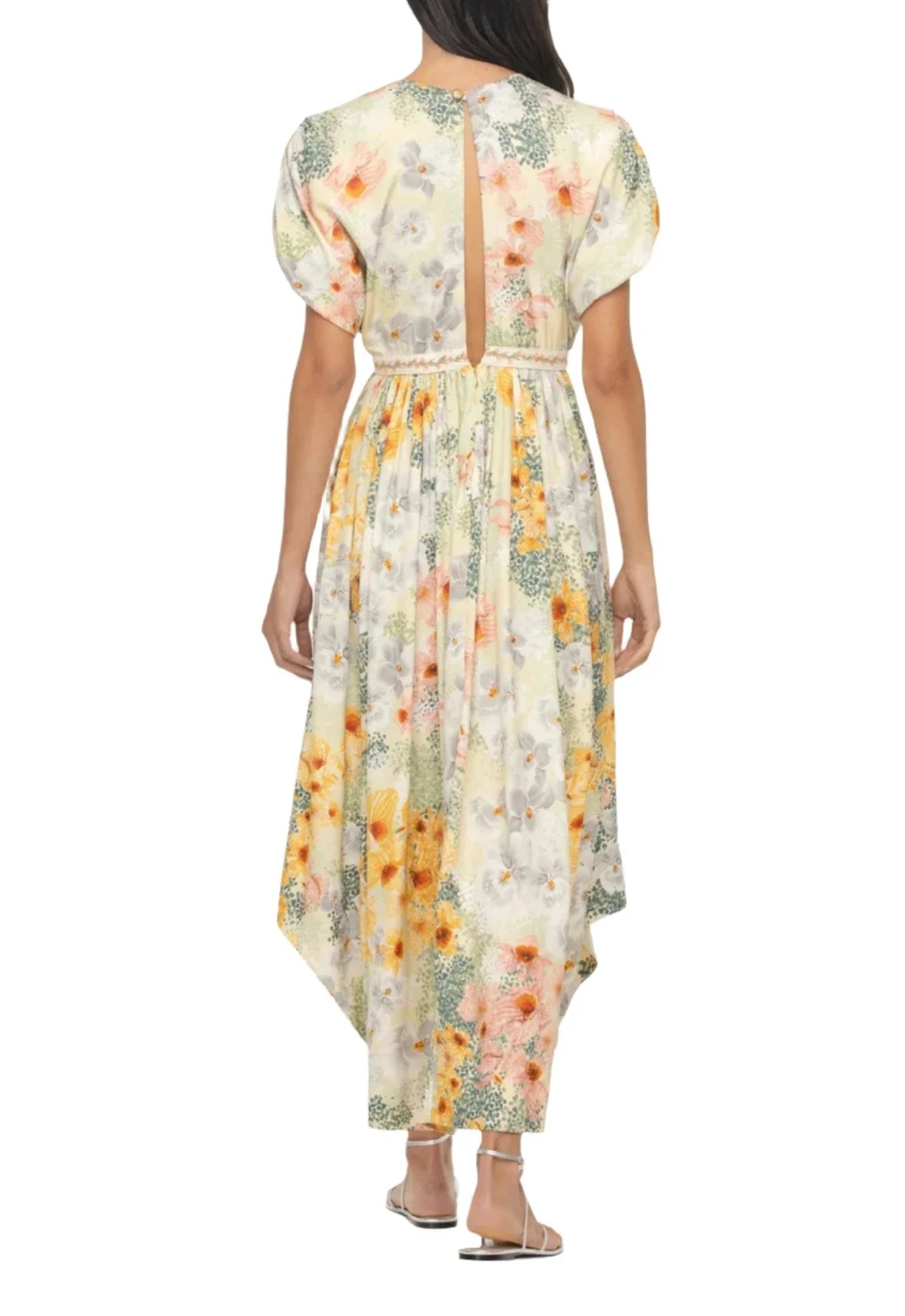 Back view of a person wearing an Agua By Aguabendita Aire Maxi Dress. This floral-print dress from Agua By Aguabendita features short puff sleeves, a high neckline, an open back, and a mid-length hem. The A-line silhouette complements the flat sandals perfectly.