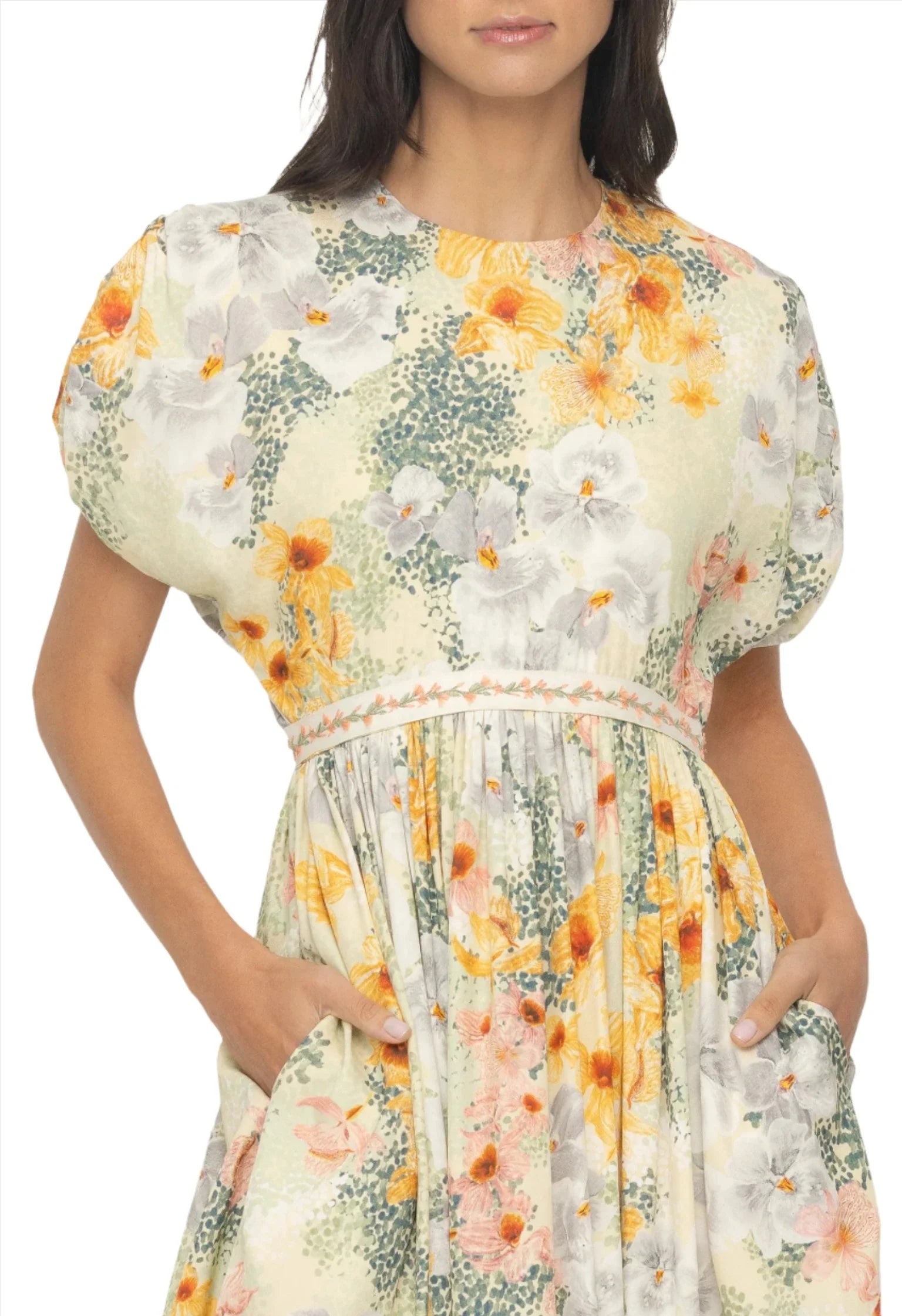 A person wearing the Agua By Aguabendita Aire Maxi Dress, a floral dress with short puffy sleeves and pockets from Agua By Aguabendita. The dress features an A-line silhouette with a mix of yellow, orange, and white flowers on a light green background.