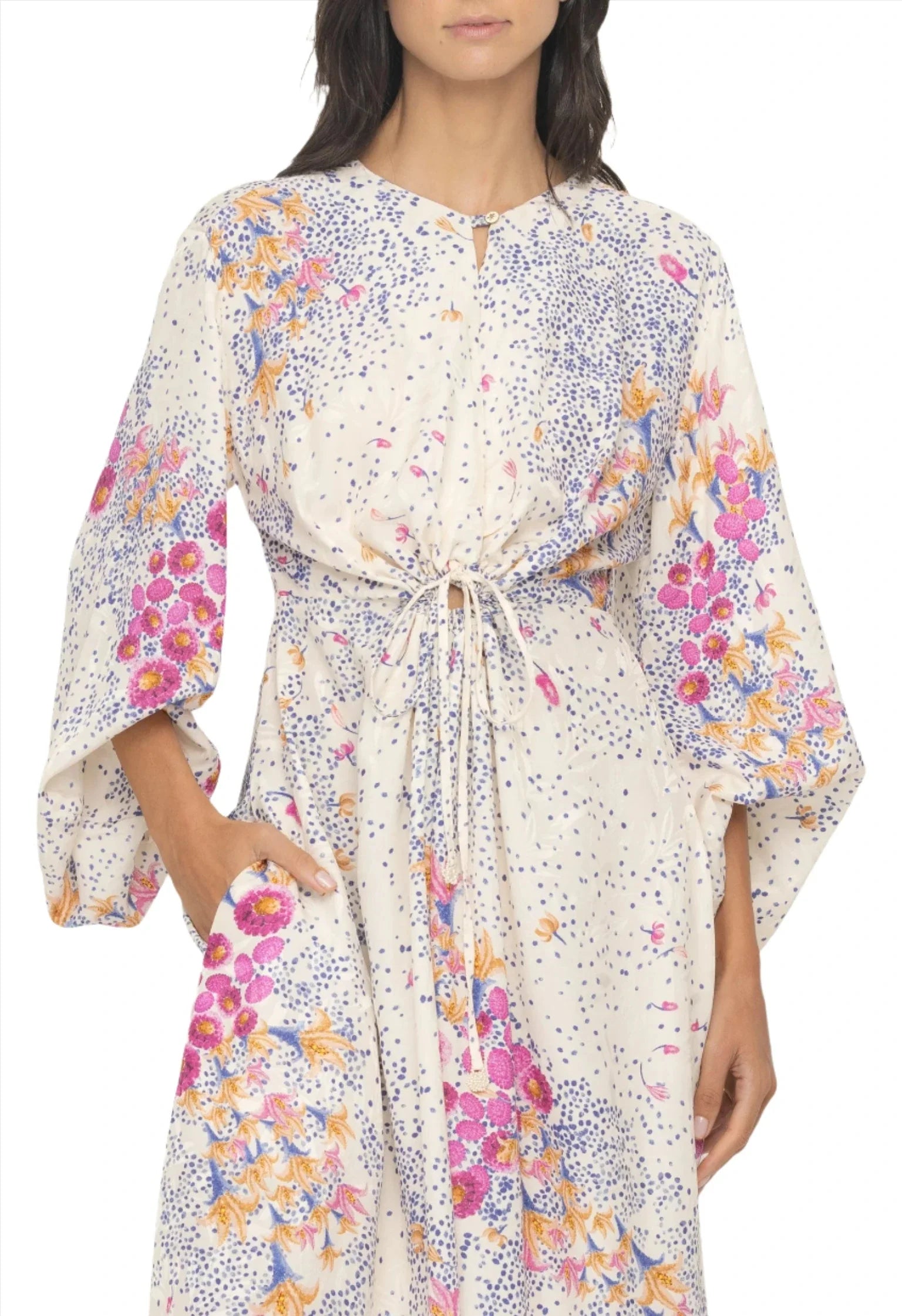 Person wearing a white floral dress with blue, orange, and pink placement print patterns. The Agua By Aguabendita Antonieta Maxi Kaftan features long sleeves and a central drawstring.