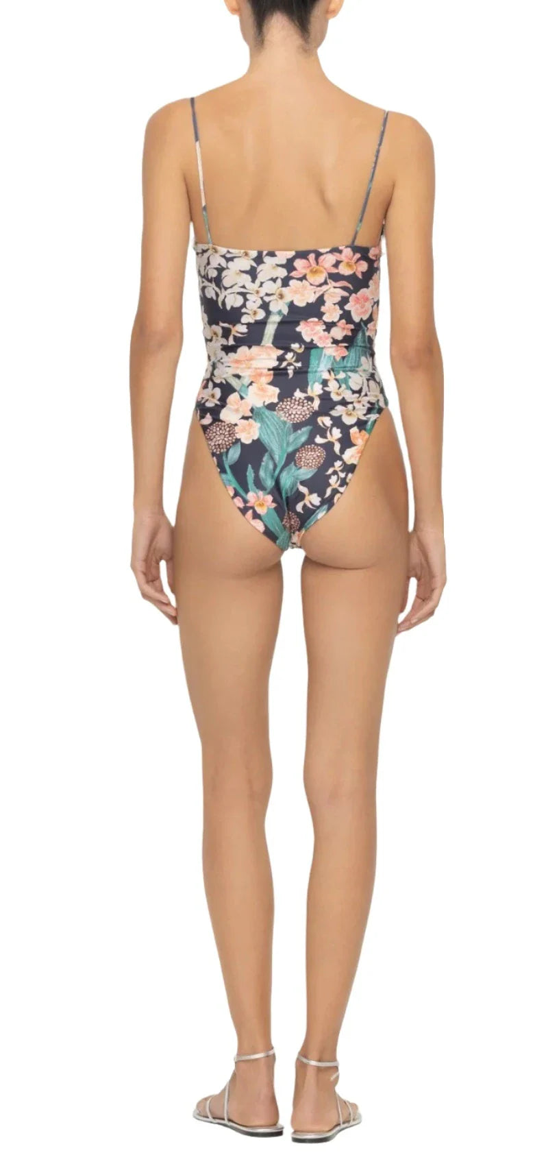 A woman models the Agua By Aguabendita Ebano One Piece swimsuit from Agua By Aguabendita, featuring a floral pattern, adjustable straps, and a heart-shaped neckline, as she stands with her back to the camera.