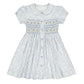The Antoinette Baby Girls' and Girls' Violette Floral Short Puff Smocked Dress exudes French elegance with white floral patterns, short sleeves, blue buttons, and a pleated skirt adorned with light blue and yellow flowers plus exquisite blue accent stitching on the bodice.