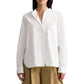 A woman wears the TWP Tied Down Shirt—a white, long-sleeve, button-down shirt in soft cotton shirting with a chest pocket—paired with a tan skirt. Her face is not fully visible.