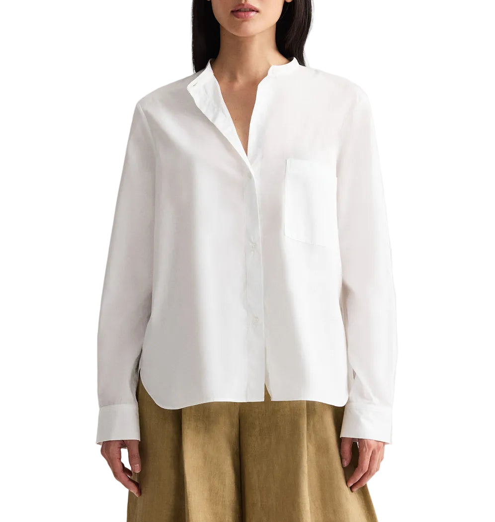 A woman wears the TWP Tied Down Shirt—a white, long-sleeve, button-down shirt in soft cotton shirting with a chest pocket—paired with a tan skirt. Her face is not fully visible.