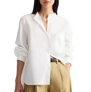 A woman wears the TWP Tied Down Shirt—a loose-fitting white button-down crafted from crisp cotton shirting—paired with beige high-waisted pants, standing with one hand in her pocket.