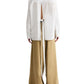 A model wears the TWP Tied Down Shirt, a white long-sleeve top with a back slit and tie detail inspired by classic cotton shirting, paired with wide-leg tan pants against a white background.