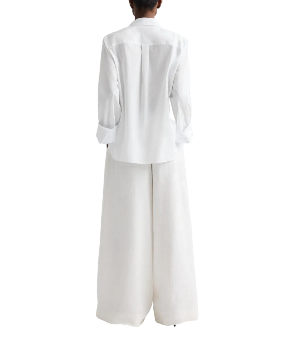 A person stands facing away against a plain white background, showcasing the TWP Next Morning Shirt—an oversized button-down styled with wide-leg white trousers for a relaxed silhouette.