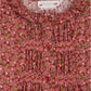 Close-up of the Bonpoint Girls' Gentille blouse, crafted from Liberty organic cotton with a floral pattern, red buttons, smocked and embroidered details, a ruffled collar, and the Bonpoint label at the neckline.