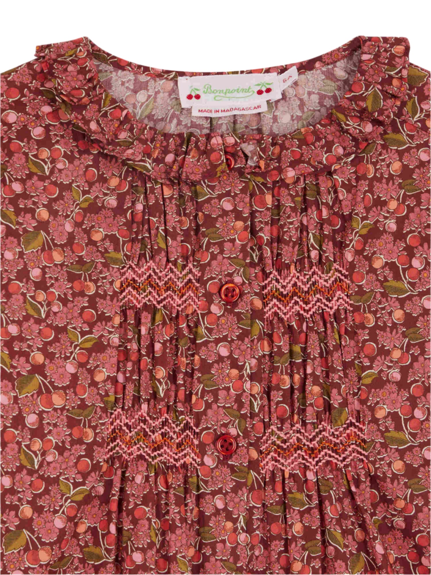 Close-up of the Bonpoint Girls' Gentille blouse, crafted from Liberty organic cotton with a floral pattern, red buttons, smocked and embroidered details, a ruffled collar, and the Bonpoint label at the neckline.