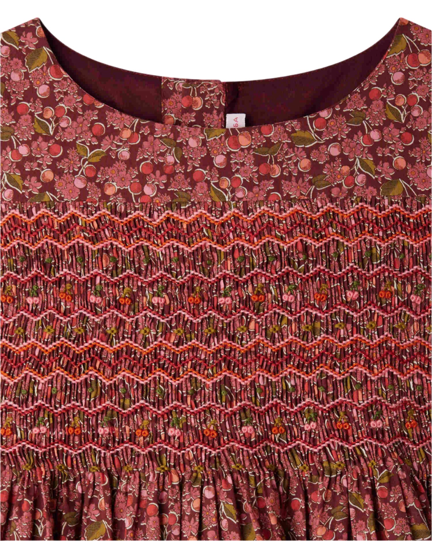 Close-up of Bonpoint's Girls' Duchesse Smocked Dress made with Liberty Fabric, showcasing a red and pink floral print, embroidered smocking on the chest, and a round neckline.