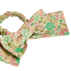 The Jeani Scrunchie in Pink Liberty Fabric by Bonpoint features a floral pattern in green, pink, and beige tones, crafted from premium Liberty fabric with an attached bow.