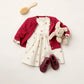 A cream dress with small red prints, a Bonpoint Baby Girls' and Girls' Jarancia cardigan with a Fancy Wool Stitch, matching red shoes, a plush bunny toy, and a wooden hairbrush are arranged on a white background.