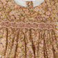 Close-up of the Bonpoint Baby Girls' and Girls' Félicie Smocked Dress made with Liberty Fabric, featuring a pink and yellow floral motif, smocked chest detailing, and a rounded neckline.