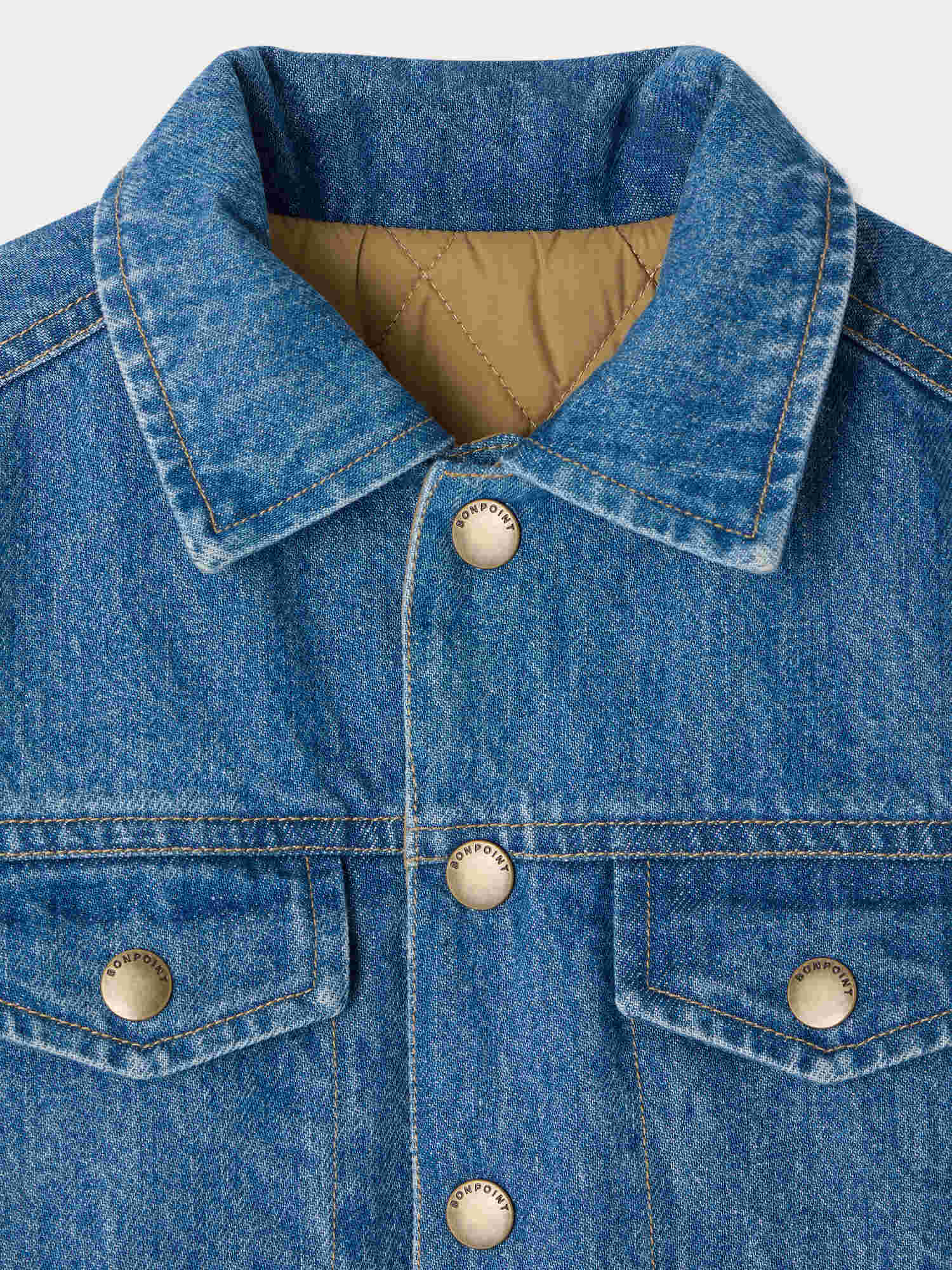 Close-up of Bonpoint’s Boys’ Marvin Reversible Jacket with Embroidery on the Back. This organic cotton denim jacket features metal snap buttons, a visible collar, chest pockets, and a tan quilted lining inside—combining classic style with comfort and durability.