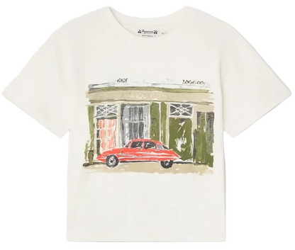 The Boys’ Eidan T-Shirt from Bonpoint is a white organic cotton tee for boys, featuring an illustration of a red car parked in front of a green building with windows and a door.